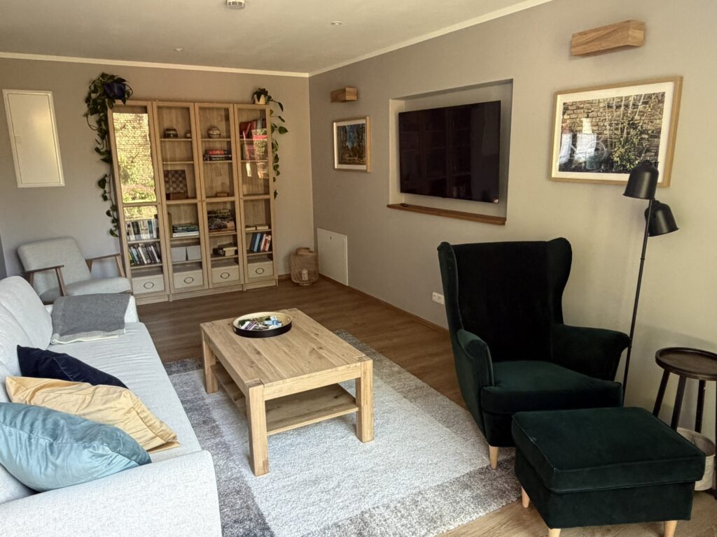 Wohnzimmer mit Sofa, Sessel, Flachbild-TV, Bücherschrank und Couchtisch